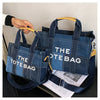 A dark blue denim tote bag with light blue stripes is shown being held by a hand.
