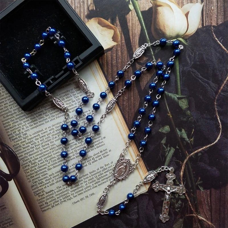 Blaue Rosenkranzkette mit Kreuzanhänger auf dunkler Fläche neben Buch und Rose