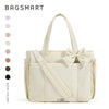 A cream-colored canvas tote bag with a bow detail and multiple pockets shown against a white background.