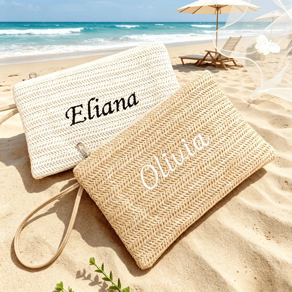 Two woven straw makeup bags labeled Eliana and Olivia resting on sandy beach near the ocean