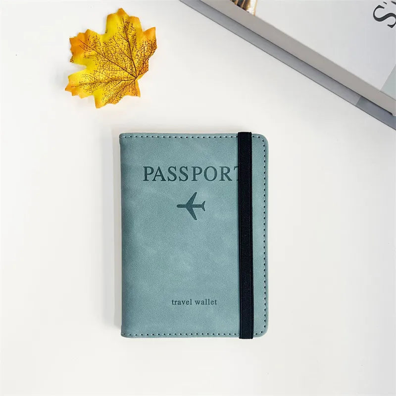 A teal passport wallet lies on a white surface next to a yellow autumn leaf.