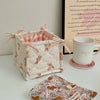 A quilted cotton storage basket with a lace flower design sits next to a white mug and a piece of fabric.