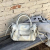 A cream-colored retro motorcycle PU leather crossbody shoulder bag resting on a wooden surface against a brick wall.