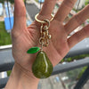 A hand holds a gold-toned crystal pear charm keychain with a green gemstone drop.