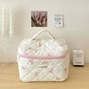 Sac de rangement cosmétique blanc matelassé avec motif nœud rose, posé sur une surface en bois à côté de bougies et d'une boî