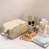 A beige PU leather travel makeup organizer with double zippers and various cosmetic bottles is displayed on a light surface.