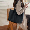 A woman holds a large black leather tote bag while standing in front of white wooden cabinets.