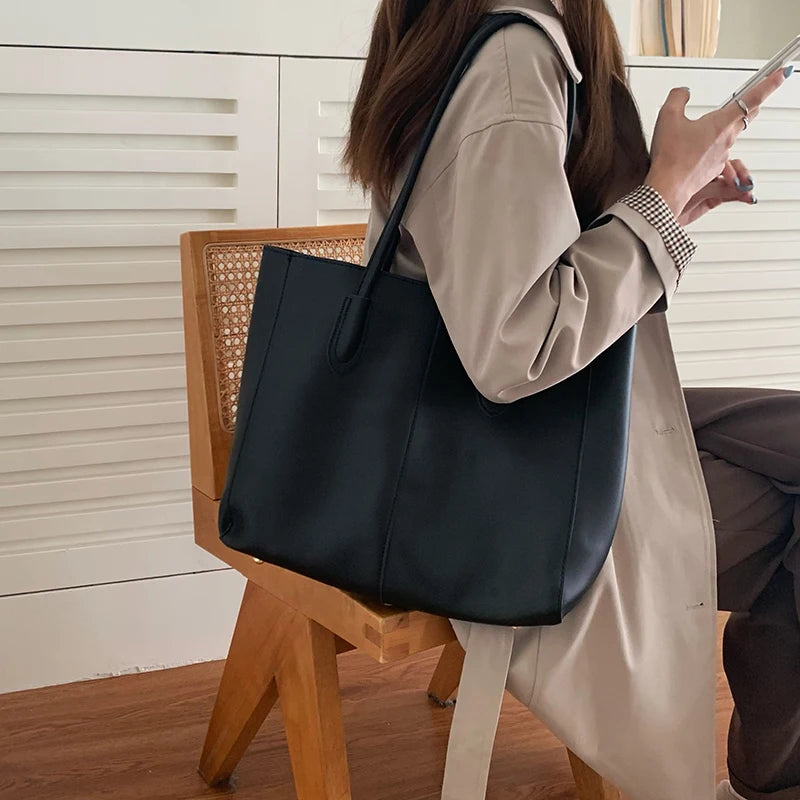 A woman holds a large black leather tote bag while standing in front of white wooden cabinets.
