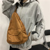 A person is holding a brown canvas crossbody shoulder bag with multiple pockets against a gray hoodie.