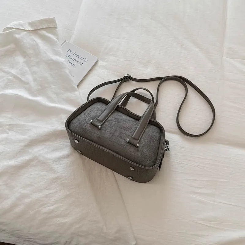 A dark gray retro crocodile textured mini crossbody bag resting on a white sheet with a small card nearby.