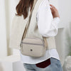 A woman is wearing a beige sleeveless vest and a light-colored shirt, carrying a beige nylon crossbody bag.