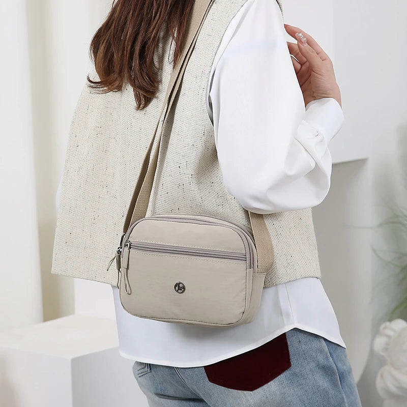 A woman is wearing a beige sleeveless vest and a light-colored shirt, carrying a beige nylon crossbody bag.