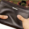 A dark brown leather mens long zipper wallet clutch being held by a hand, with a background of cattle.