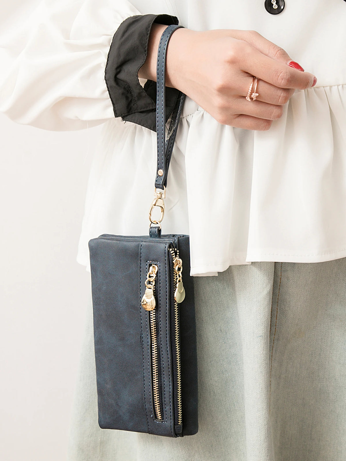 A dark blue retro long wallet with a double zipper is held by a person wearing a white blouse.