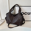 Un sac fourre-tout en cuir marron foncé avec une sangle d'épaule, exposé sur une surface blanche.
