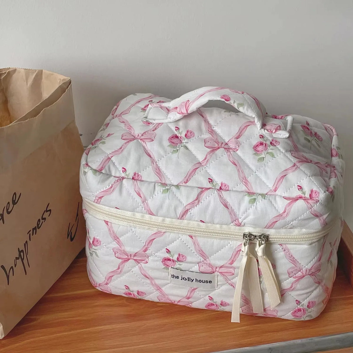 A white floral embroidered makeup bag with pink accents resting on a wooden surface.