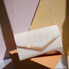 A light pink glitter pleated crossbody clutch bag with a gold chain hanging against a soft background.