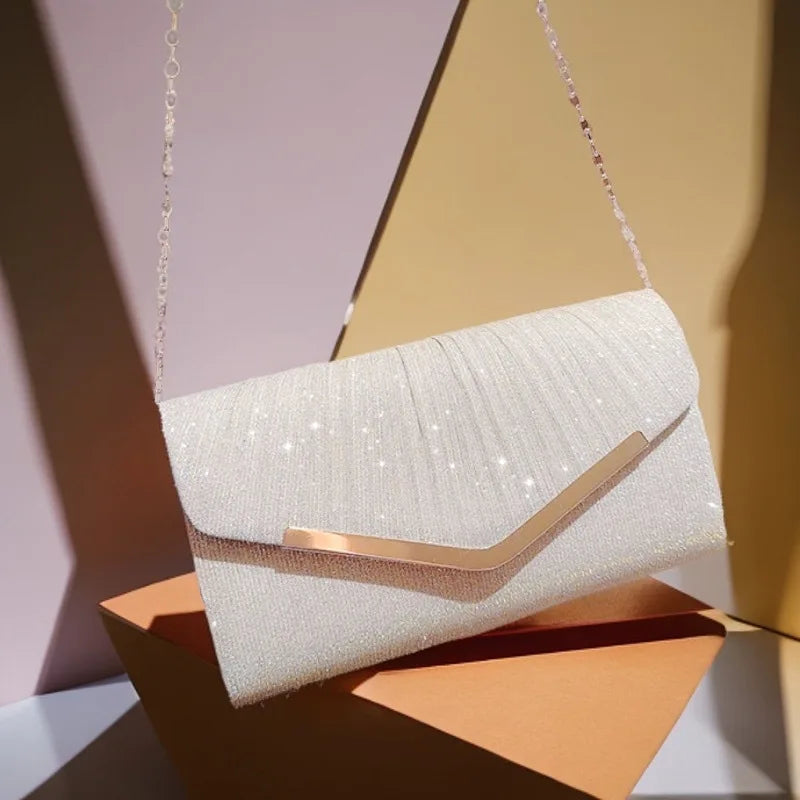A light pink glitter pleated crossbody clutch bag with a gold chain hanging against a soft background.