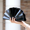 A hand holds an open gold acrylic chain crossbody bag displaying multiple layered black acrylic panels.