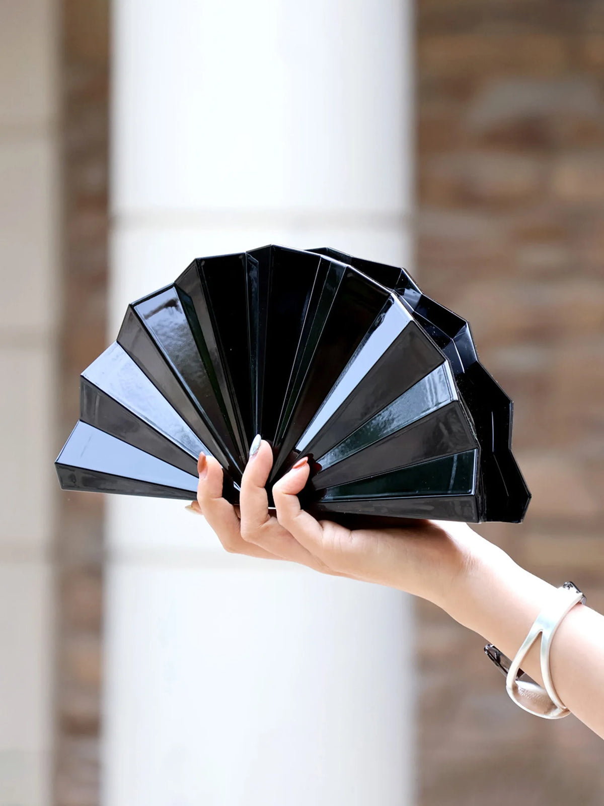 A hand holds an open gold acrylic chain crossbody bag displaying multiple layered black acrylic panels.