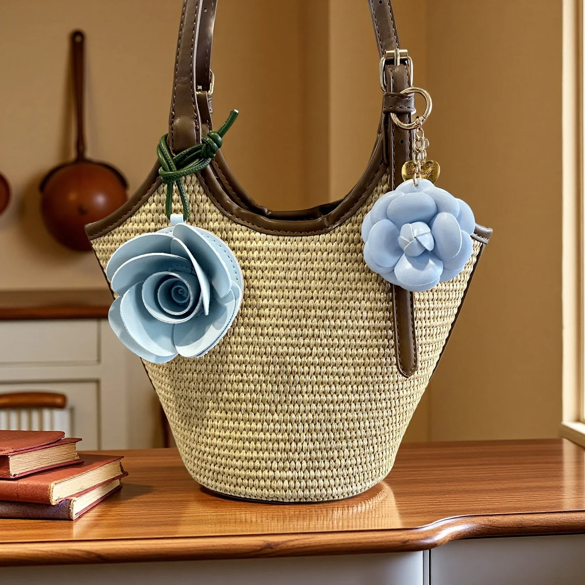 A beige woven leather bag with a brown strap and light blue floral fabric charms resting on a wooden surface.
