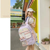 A young woman wearing a light pink Candy Color Campus backpack standing in front of a yellow storefront.