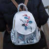 A light gray linen backpack featuring pink and blue floral embroidery carried by a person.