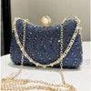 A dark blue rhinestone clutch bag with gold chain detailing and a pearl embellishment