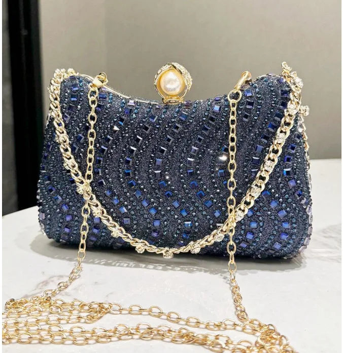 A dark blue rhinestone clutch bag with gold chain detailing and a pearl embellishment