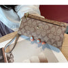 A close-up of a taupe patterned zippered wallet with gold hardware being held by a hand on a wooden surface.