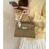 A woman holds a beige PU leather crossbody clutch bag and a smartphone against a light background.