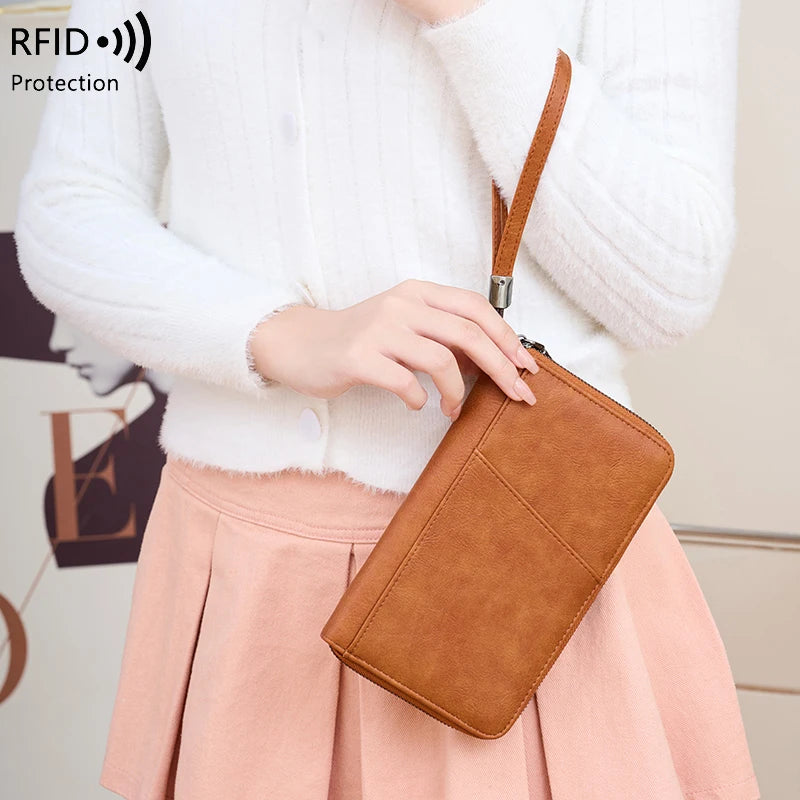 A person is holding a brown leather RFID blocking travel wallet against a pink pleated skirt.