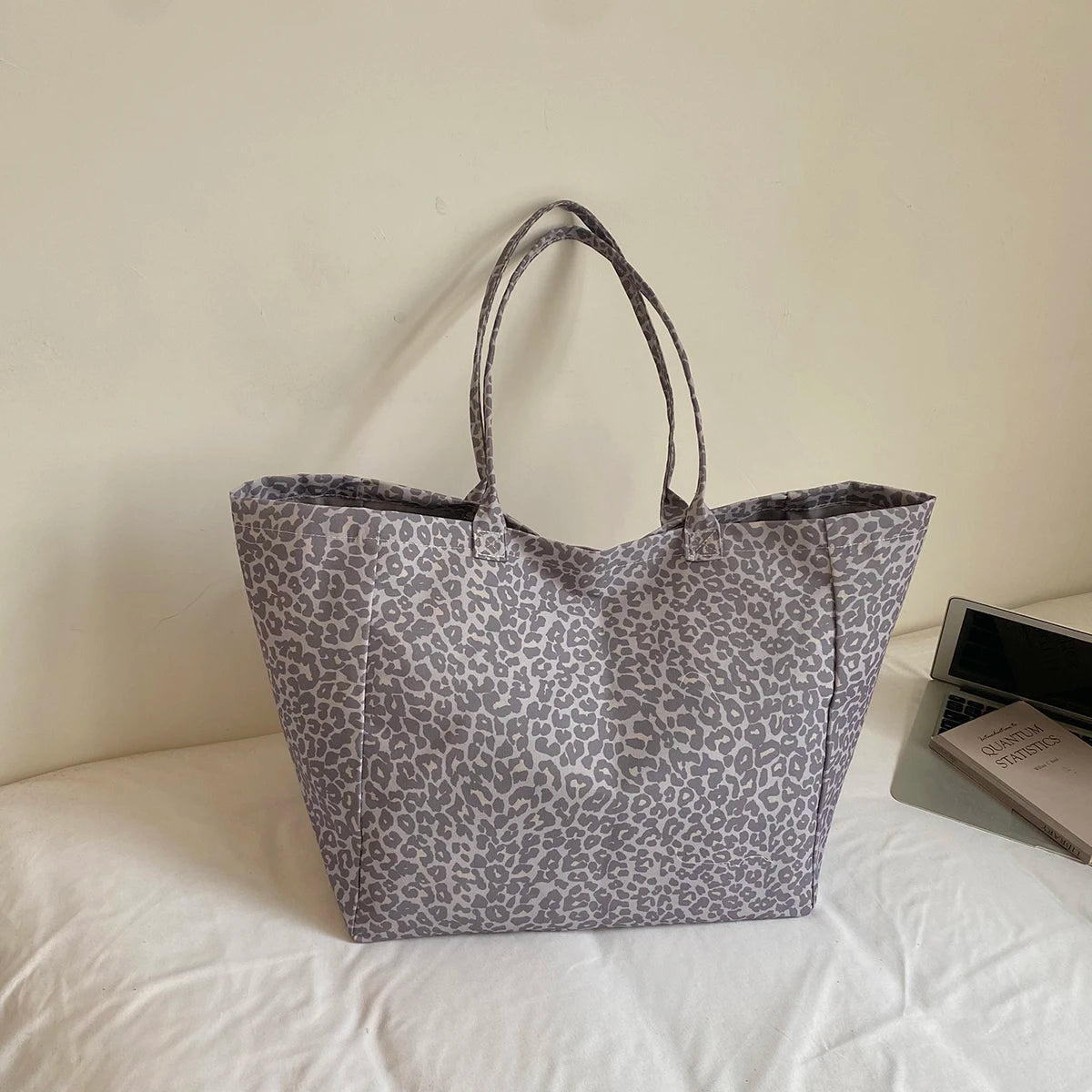 A gray leopard print canvas tote bag with handles resting on a white surface.