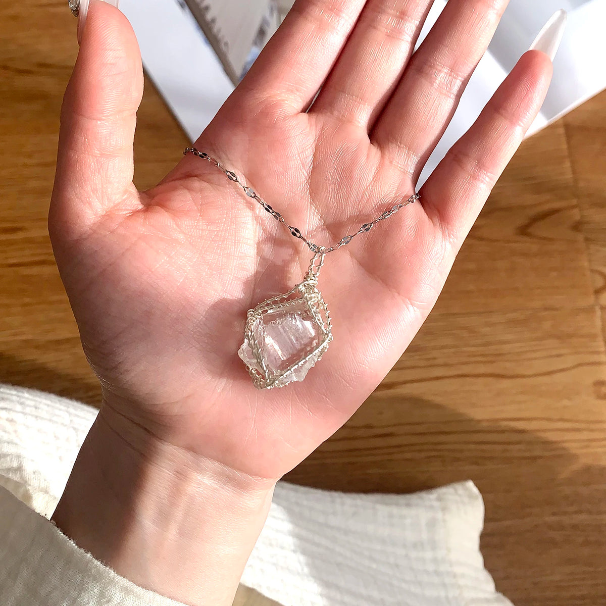 A hand holds a handcrafted amethyst crystal pendant necklace featuring a clear quartz stone wrapped with copper wire.