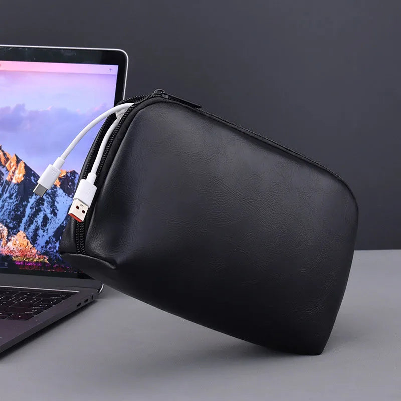 Black leather multi-layer cable organizer pouch next to a laptop.