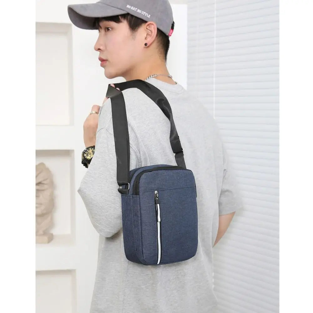 A man wearing a grey t-shirt holds a dark blue waterproof crossbody bag with black straps.