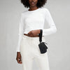 A woman wearing a white long-sleeve top and pants, holding a black nylon wristlet pouch.
