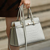 A woman holds a light gray quilted leather shoulder bag with gold hardware against a neutral background.
