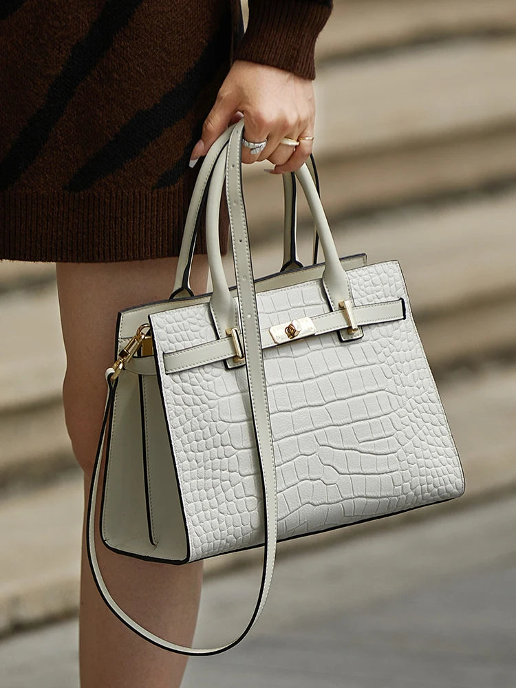 A woman holds a light gray quilted leather shoulder bag with gold hardware against a neutral background.