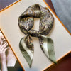 A silk paisley scarf tied in a bow, featuring olive green and beige tones, displayed on a light surface.