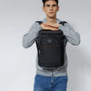 A young man wearing a grey sweatshirt and jeans is holding an Insulated Thermal Cooler Backpack on his shoulders.
