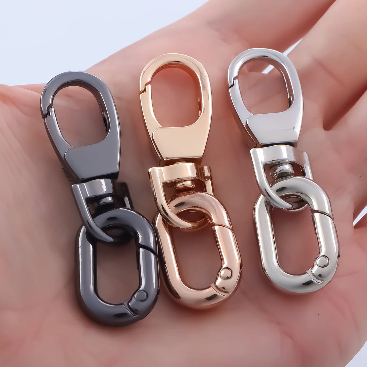 Three metal swivel lobster claw clasps in silver, gold, and black are shown on a hand.