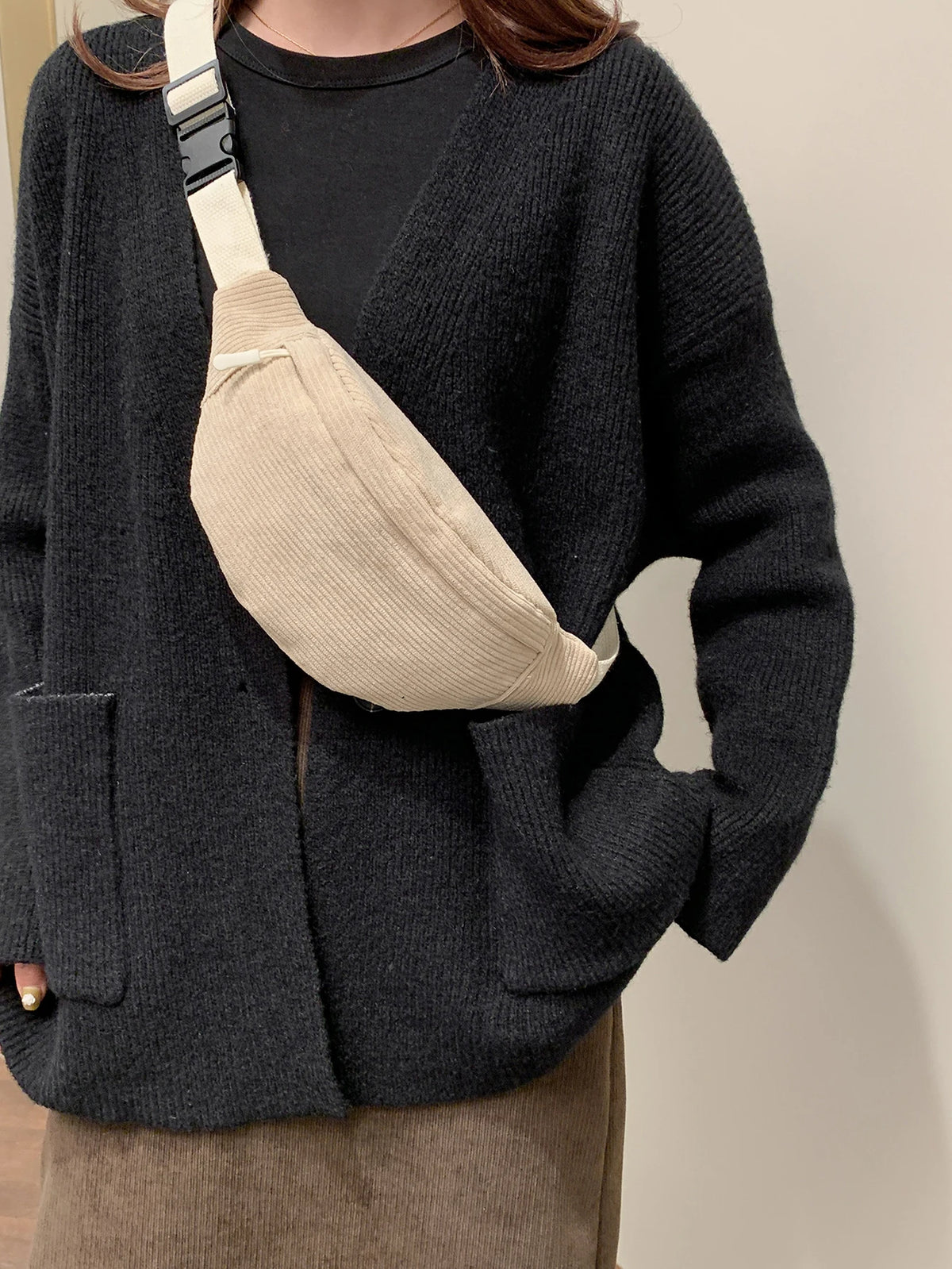 A dark gray knitted cardigan with a beige nylon crossbody sling bag worn across the chest.