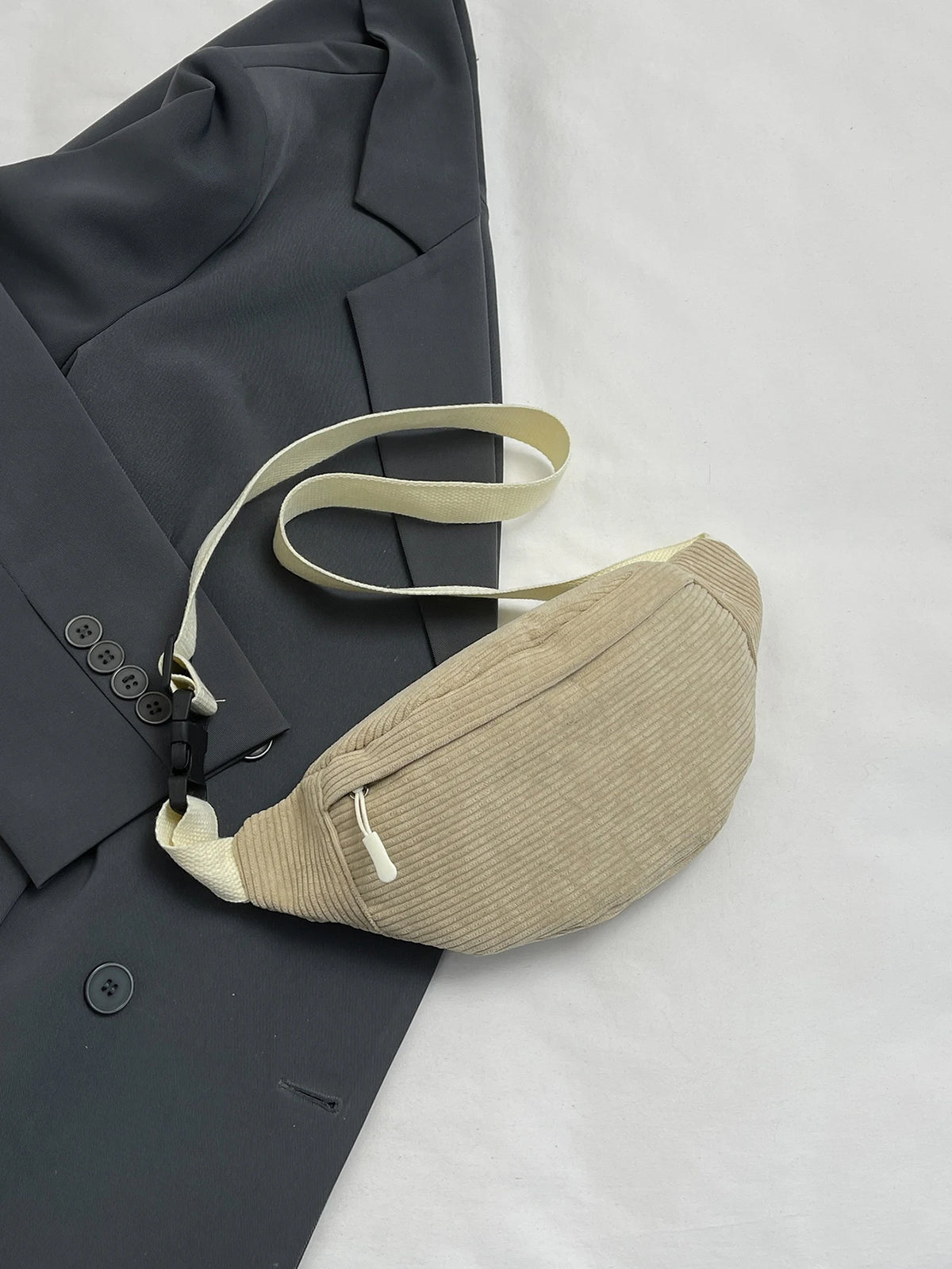 A light beige nylon crossbody sling bag is shown resting on a dark gray blazer.