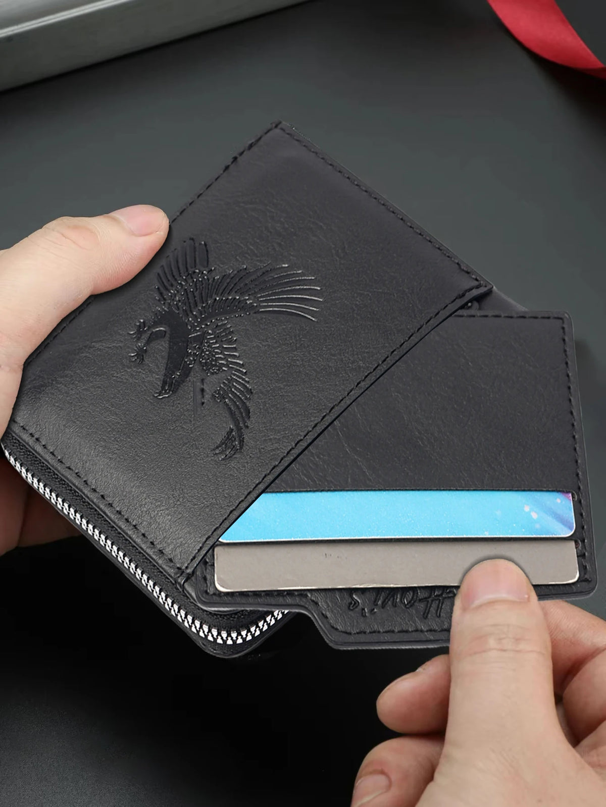 A hand holds a black embossed PU leather slim wallet with a silver card inside.