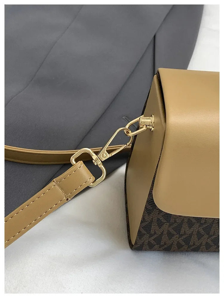 A tan Michael Kors letter square crossbody bag with gold hardware shown against a gray fabric background.