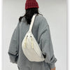 A woman wearing a gray sweatshirt and a maroon beanie is carrying a cream corduroy waist pack.