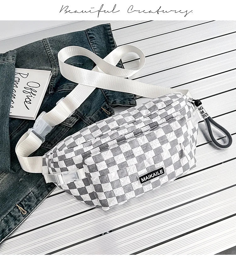 A plaid checkered crossbody chest bag in gray and white with a white adjustable strap resting on a wooden surface.