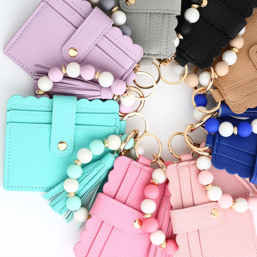 A collection of silicone bead and leather card wallets in various pastel colors like pink, mint green, blue, and beige.