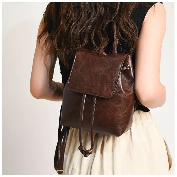 Une femme vue de dos portant un mini sac à dos en cuir marron avec un haut de tissu clair.